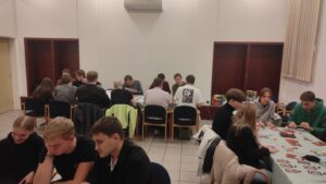 Zdjęcie przedstawia dużą ilość osób siedzących przy stolikach, którzy grają w planszówki