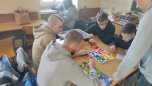 Zdjęcie przedstawia kilka osób wspólnie grających w grę planszową przy jednym stole