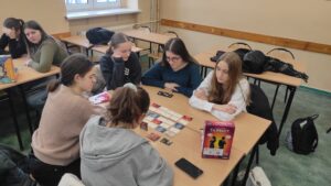 Zdjęcie przedstawia kilku uczestników grających w planszówkę przy jednym stoliku