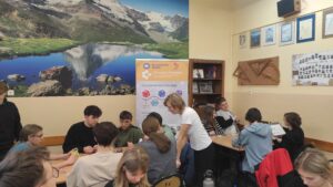 Zdjęcie przedstawia kilka osób grających w planszówki, pomocnika oraz rollup prezentacyjny