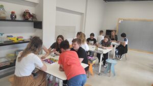 Zdjęcie przedstawia dużą ilość dzieci grających w planszówki przy kilku stołach w sali lekcyjnej