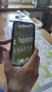 Zdjęcie przedstawia telefon którego kamera skierowana jest w stronę planszy do gry która sprawia, że w telefonie włączają się wirtualne elementy do gry za pomocą technologii AR