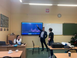 Zdjęcie przedstawia prezentera pokazującego wykres oraz uczestników warsztatów którzy siedzą przy ławkach klasowych