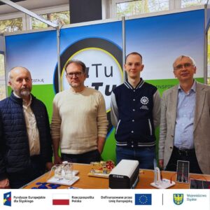 Czterech pracowników Politechniki stoi przy stanowisku piknikowym. Na stanowisku porozstawiane są urządzenia wykorzystujące odnawialne źródła energii. Kliknięcie powoduje zwiększenie zdjęcia.