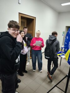 Uśmiechnięte osoby przy stanowisku Politechniki Śląskiej. Obok na stole rozłożone są gadżety reklamowe. Kliknięcie powoduje zwiększenie zdjęcia.