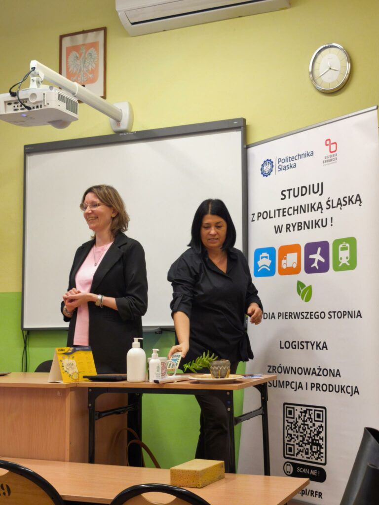 Dwie kobiety stoją przy tablicy, jedna z nich trzyma w ręku pilota. Kliknięcie powoduje zwiększenie zdjęcia.