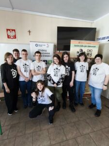 Organizatorzy spotkania pozują do wspólnego zdjęcia na tle banerów promocyjnych. Kliknięcie powoduje zwiększenie zdjęcia.