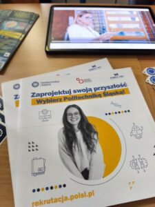 Na stole leży informator Politechniki oraz tablet wyświetlający reklamę uczelni. Kliknięcie powoduje zwiększenie zdjęcia.