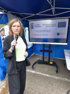 Aldona Rosner wygłasza prezentację pod namiotem. W tle wyświetlany jest na ekranie plakat informacyjny projektu COZEiTW. Kliknięcie powoduje zwiększenie zdjęcia.