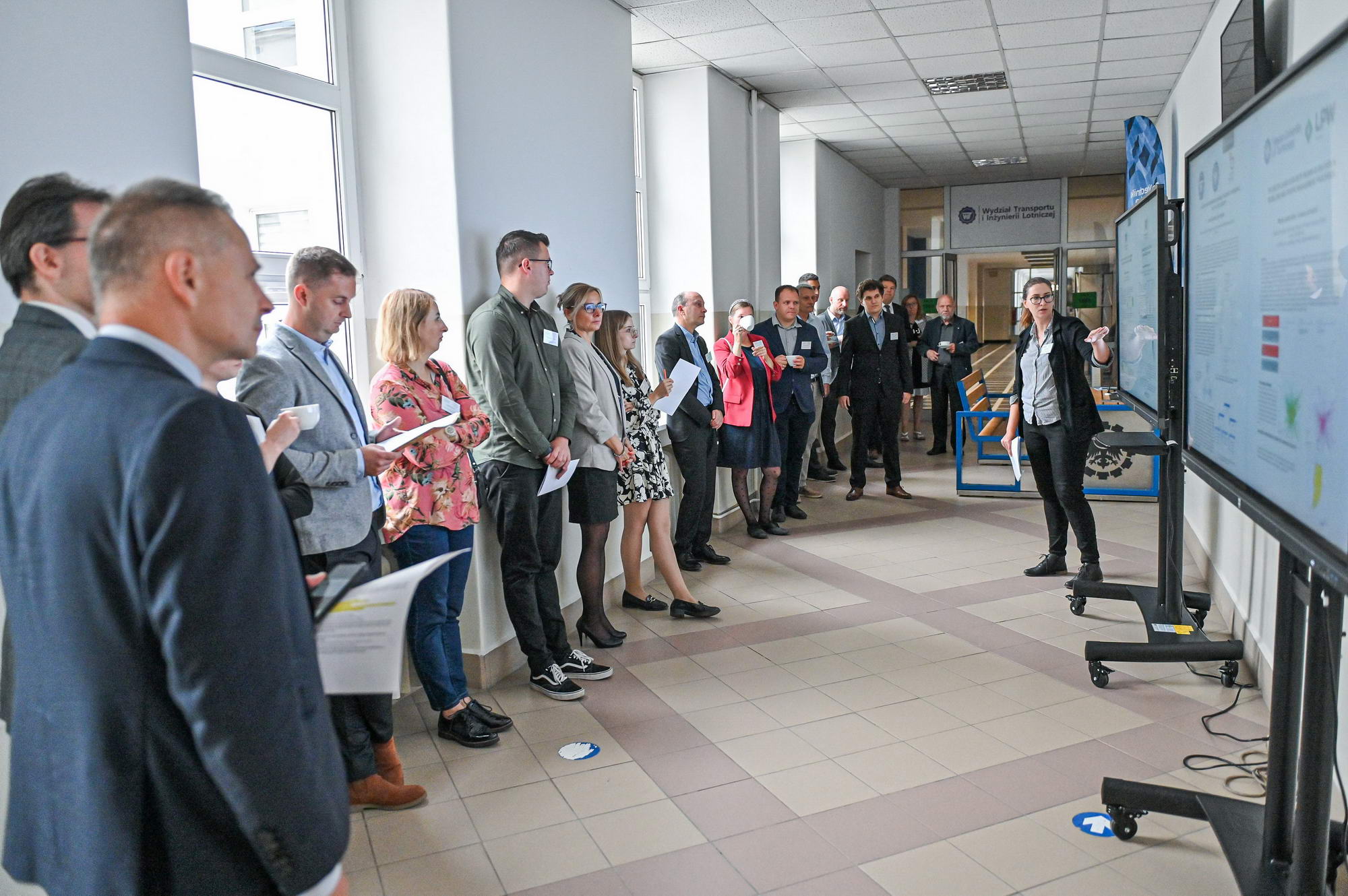 uczestnicy konferencji przed monitorami na korytarzu