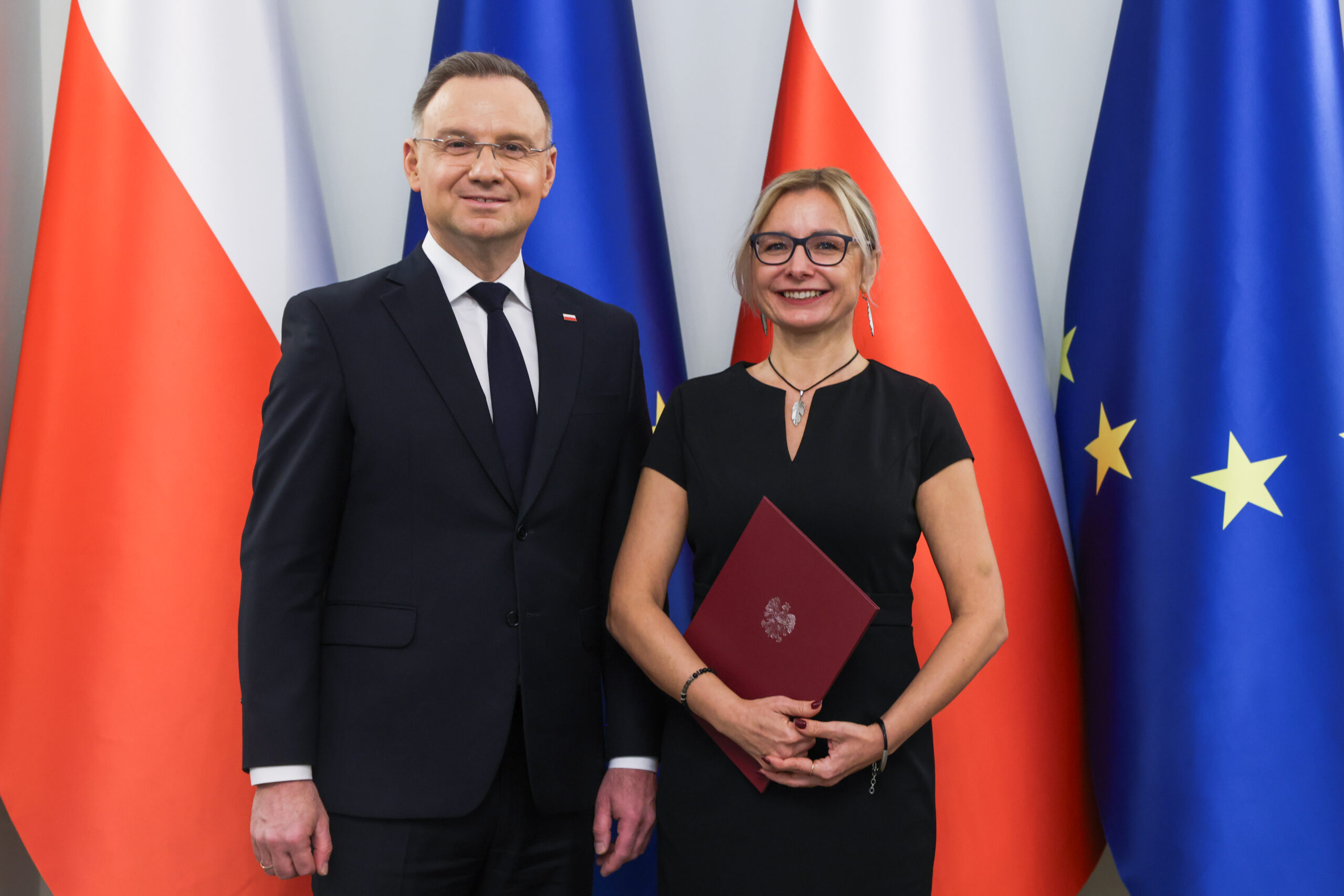 Prezydent Andrzej Duda i prof. Dorota Burchart na tle flag polskich i unijnych