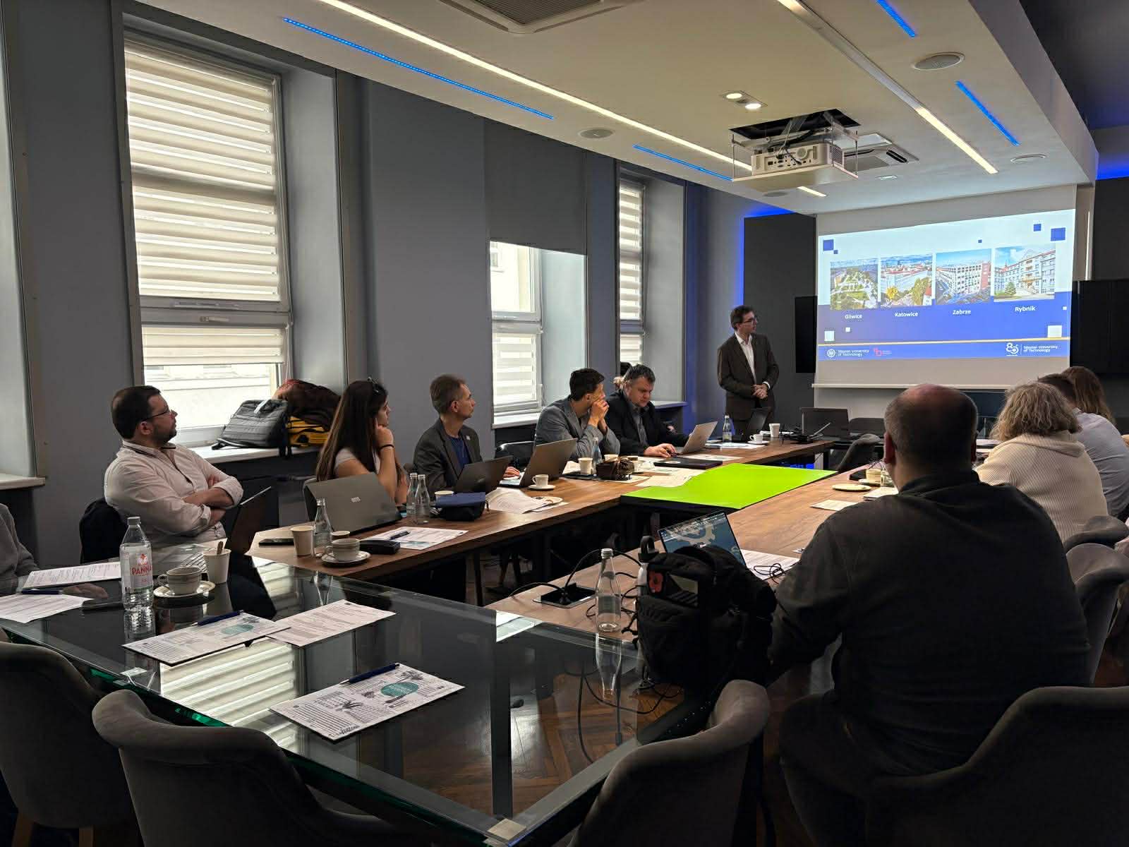 uczestnicy projektu siędzą przy stołach w sali 1023, dziekan wyświetla prezentację na ekranie
