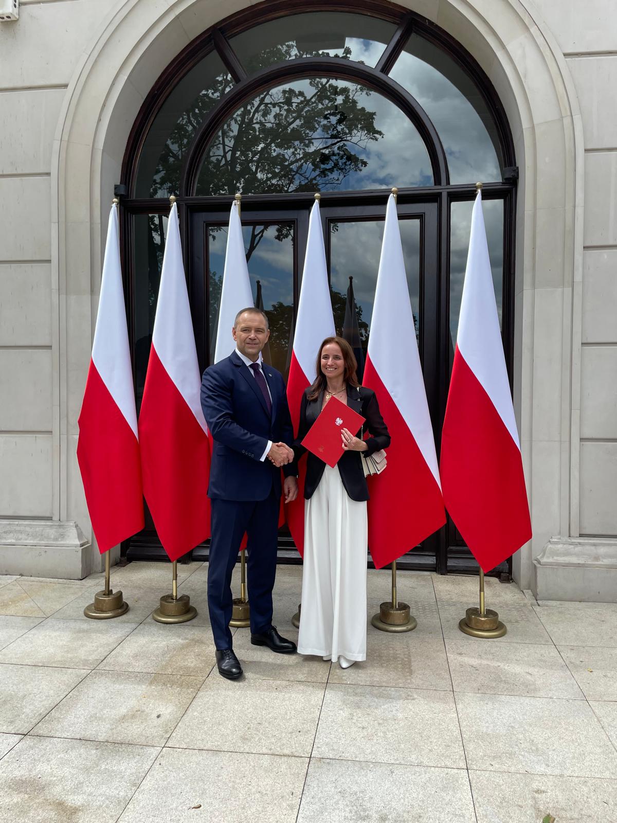 Prof. Bożena Szczucka-Lasota pozuje do fotografii z Prezedentem RP Karolem Nawrockim na tle flag w barwach narodowych przed budynkiem