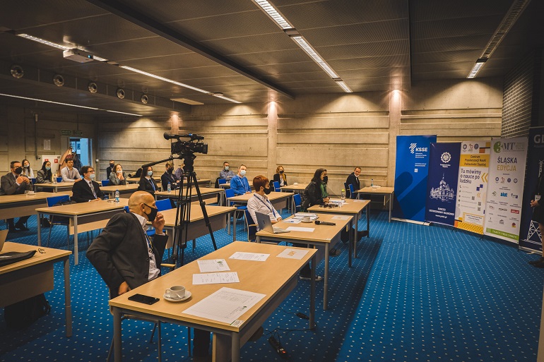 Na zdjęciu widzimy sale konferencyjną w której stoją ławki. W ławkach siedzą uczestnicy konkursu i słuchają wykładu. W Sali stoją również bannery uczelni