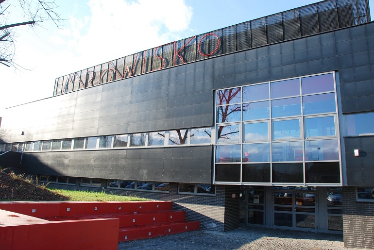 Na zdjęciu widzimy budynek Centrum Kultury Studenckiej Mrowisko. Jest czarna bryła z przeszkleniami i czerwonym napisem na górze Mrowisko