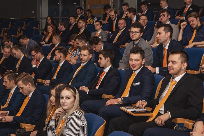 Na zdjęciu widzimy grupę studentów siedzących w auli na konferencji eDUAL. Wszyscy mają pomarańczowe krawaty