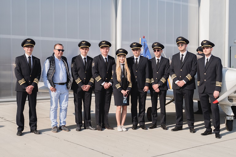 Na zdjęciu widzimy grupę pilotów w mundurach stających na tle samolotu AT 3. Za nimi hangar lotniska