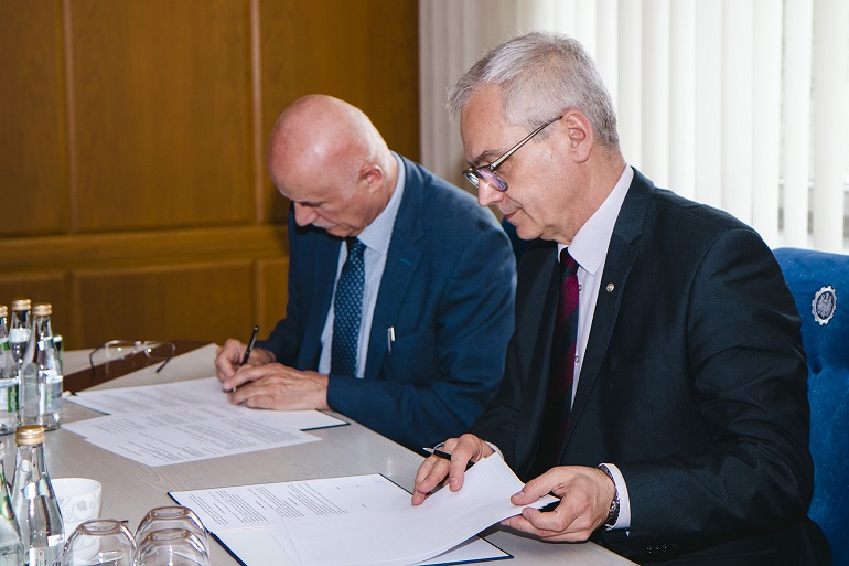 Zdjęcie przedstawia dwóch mężczyzn siedzących przy stole i podpisujących umowę o współpracy.