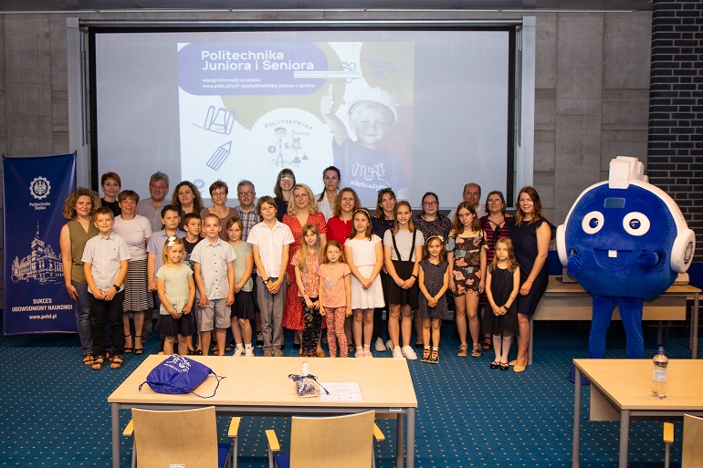 Na zdjęciu widzimy uczestników Politechniki Juniora. Wraz z nimi po prawej stronie stoi niebieska maskotka Politechniki Śląskiej Poliś