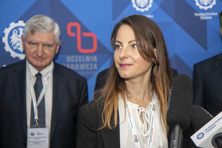 Zdjęcie przedstawia kobietę, za nią stoi mężczyzna.