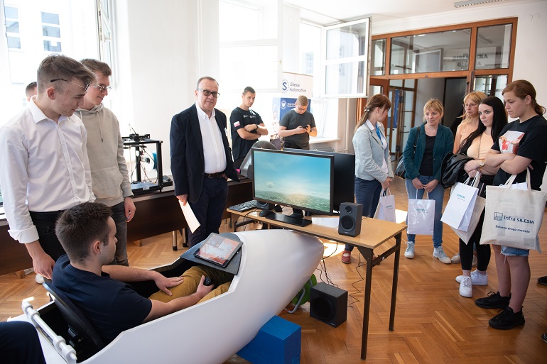 Na zdjęciu widzimy studentów i wykładowcę w Sali wykładowej. Stoją i oglądają bolida