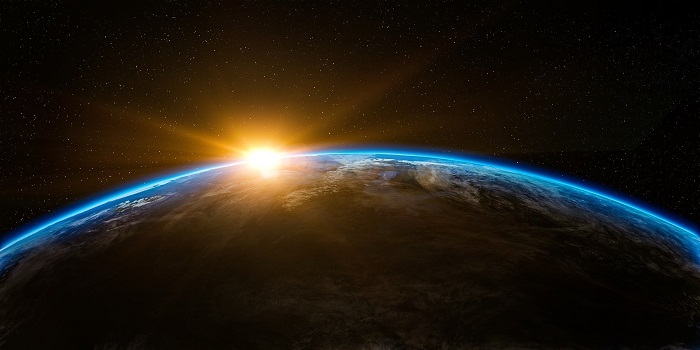 Obrazek przedstawia widok Ziemi z kosmosu, za którą przebijają się promienie wschodzącego słońca..