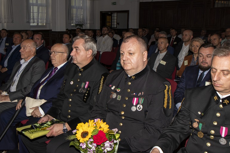 Na zdjęciu widźmy uczestników konferencji siedzących na Sali. Na pierwszym planie trzech z nich ubranych jest w stroje galowe górnika