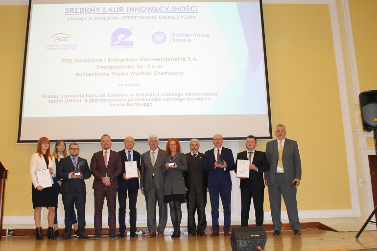 Na zdjęciu widzimy laureatów konkursu stojących na scenie Nad nimi ekran z nazwą projektu i jej twórcami
