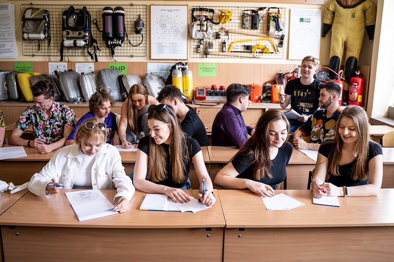 Zdjęcie przedstawia grupę studentów siedzących przy stołach.