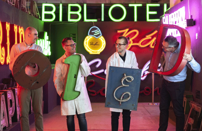 Zdjęcie przedstawia czterech naukowców w białych fartuchach, na tle neonów.