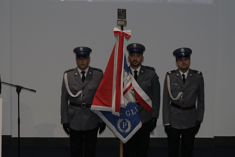 Na zdjęciu widzimy trzech policjantów stojących obok siebie, jeden z nich trzyma sztandar policji.