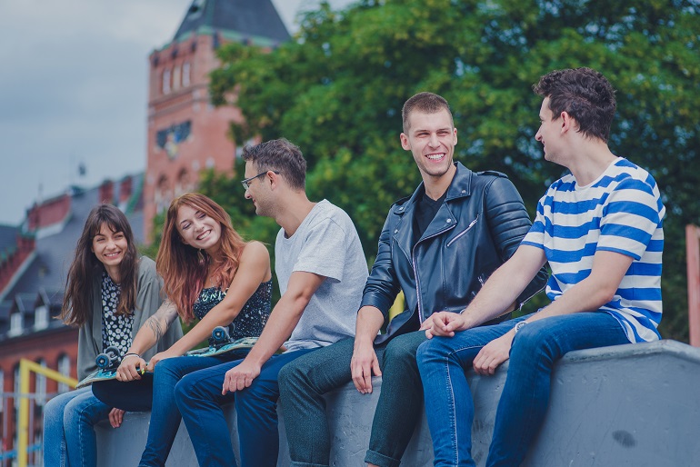 Na zdjęciu widzimy roześmianych studentów dwie dziewczyny i dwóch chłopaków siedzących na terenie kampusu Politechniki śląskiej.