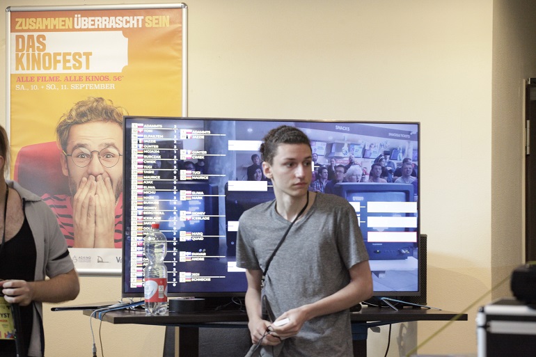 Na zdjęciu widzimy Adama Matysa siedzącego tyłem do dużego ekranu telewizora na którym widać klasyfikacje zawodów
