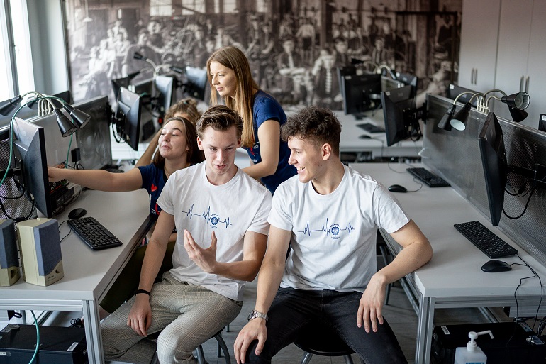 Na zdjęciu widzimy kilku studentów i studentek w pracowni komputerowej