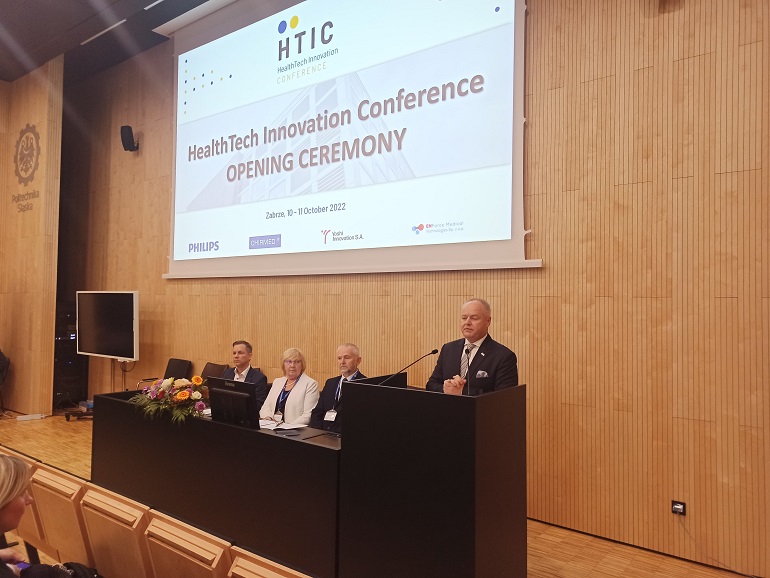 Na zdjęciu widzimy scenę w Sali konferencyjnej. Za stołem siedzi trzech prelegentów za pulpitem jeden z nich przemawia