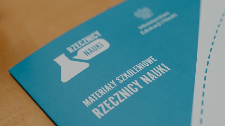 na nienieskim tle grafiki widzimy biały napis Rzecznicy Nauki w Terenie