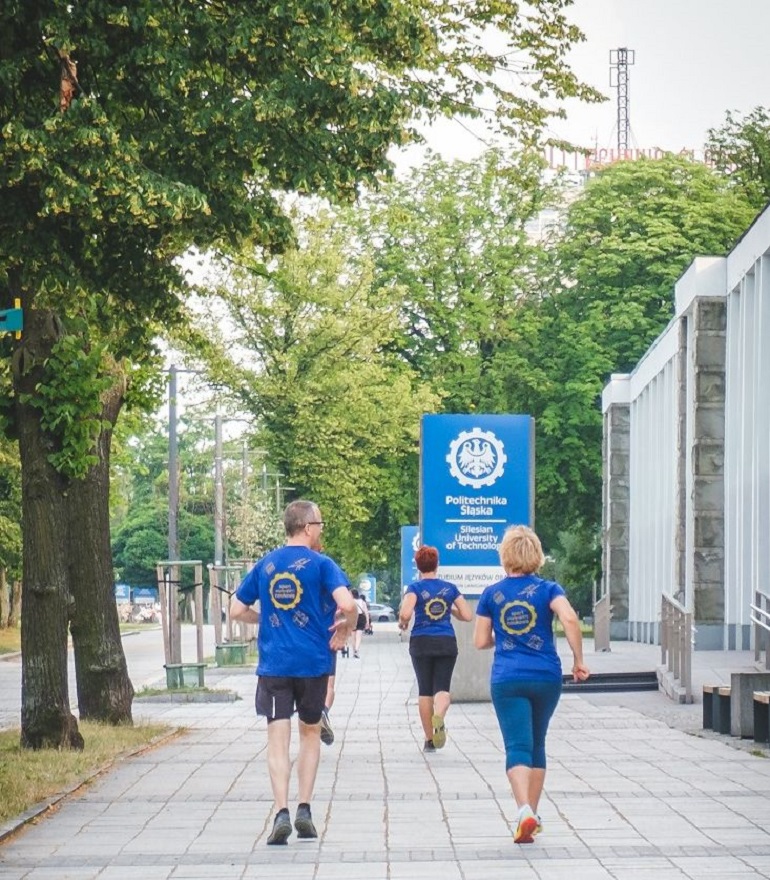 Na zdjęciu widzimy trzech biegaczy odwróconych tyłem biegnących na terenie kampusu Politechniki Śląskiej.