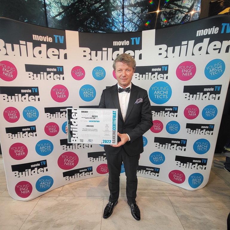 Na zdjęciu widzimy dziekana Frossa stojącego na tle ścianki z napisami Builder. Dziekan trzyma w ręku nagrodę od Buildera w postaci dyplomu