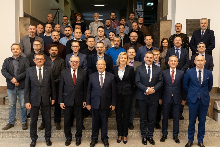 Na zdjęciu widzimy grupę około 30 osób pozujących do wspólnego zdjęcia na schodach w holu wydziału