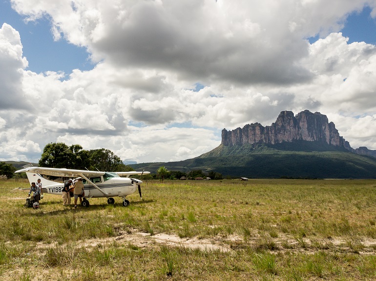 Na zdjęciu widzimy kadr z wyprawy w Ameryce Południowej. Na pierwszym planie mały samolot na drugim góra i zachmurzone niebo