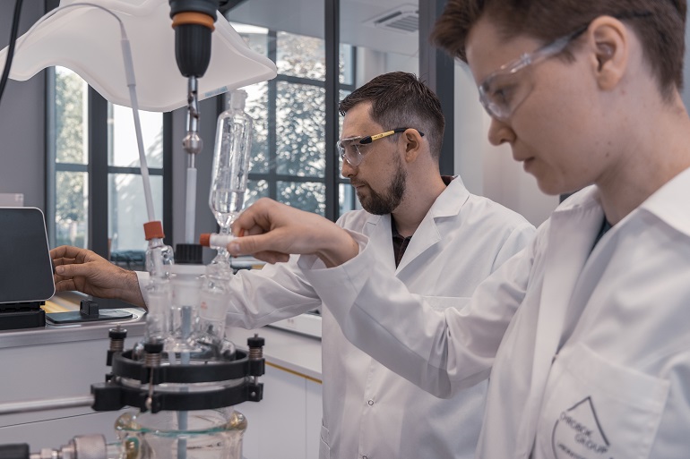Na zdjęciu widzimy dwóch studentów w białych fartuchach, którzy pracują w laboratorium