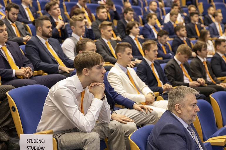 Na zdjęciu widzimy studentów w pomarańczowych krawatach i apaszkach siedzących w auli