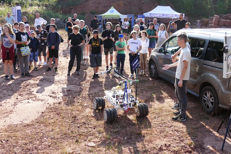 Na zdjęciu widzimy uczetnikow spotkania a na ziemi trzy małe roboty
