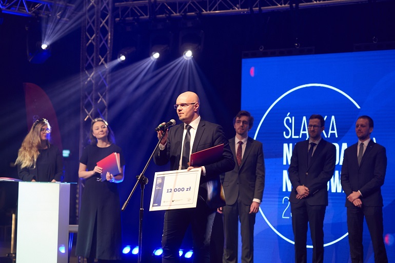 Na zdjęciu profesor Simka przemawia na scenie w ręku trzyma duży dyplom z kwotą nagrody
