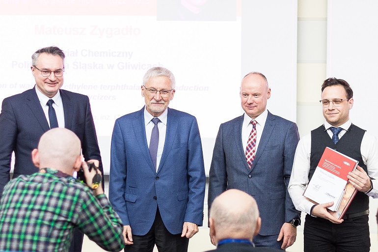 na zdjęciu student Zygadło z organizatorami konkursu. Student trzyma w rękach rozłożony dyplom
