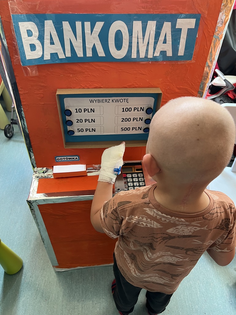 na zdjęciu mały chłopczyk przy zabawkowym bankomacie