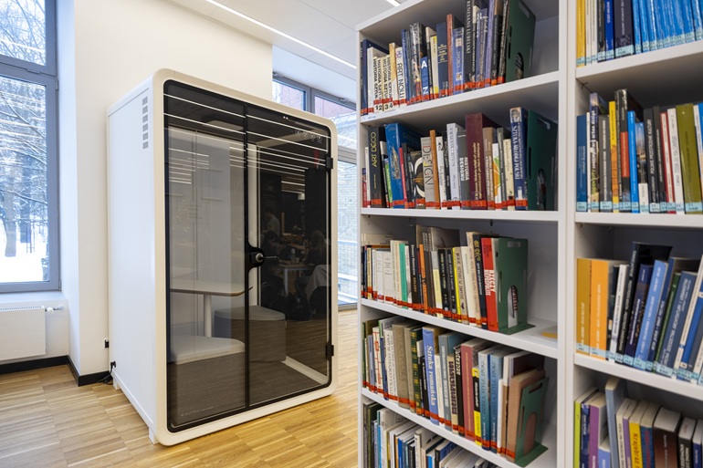 na zdjęciu kabina akustyczna a na pierwszym planie regał z książkami