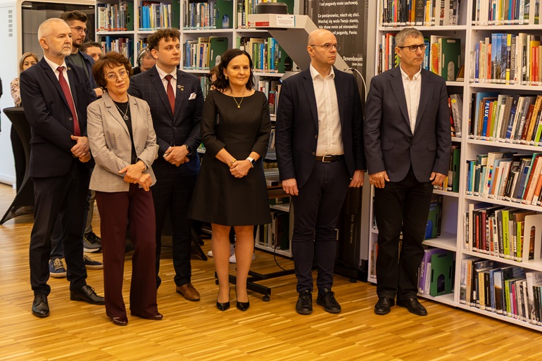 na zdjęciu grupa osób stojących przy regałach z książkami