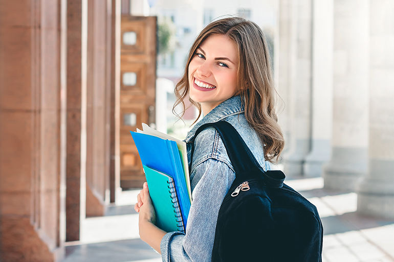 Young girl student smiling against university. Cute girl student holds folders and notebooks in hands. Learning, education concept